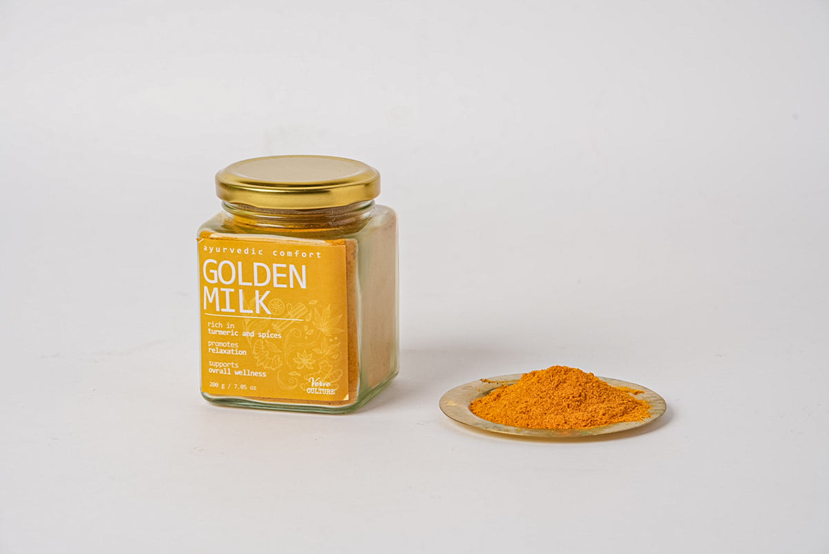 Glass jar with golden lid containing golden milk spice blend powder, with loose powder displayed on small wooden plate beside
