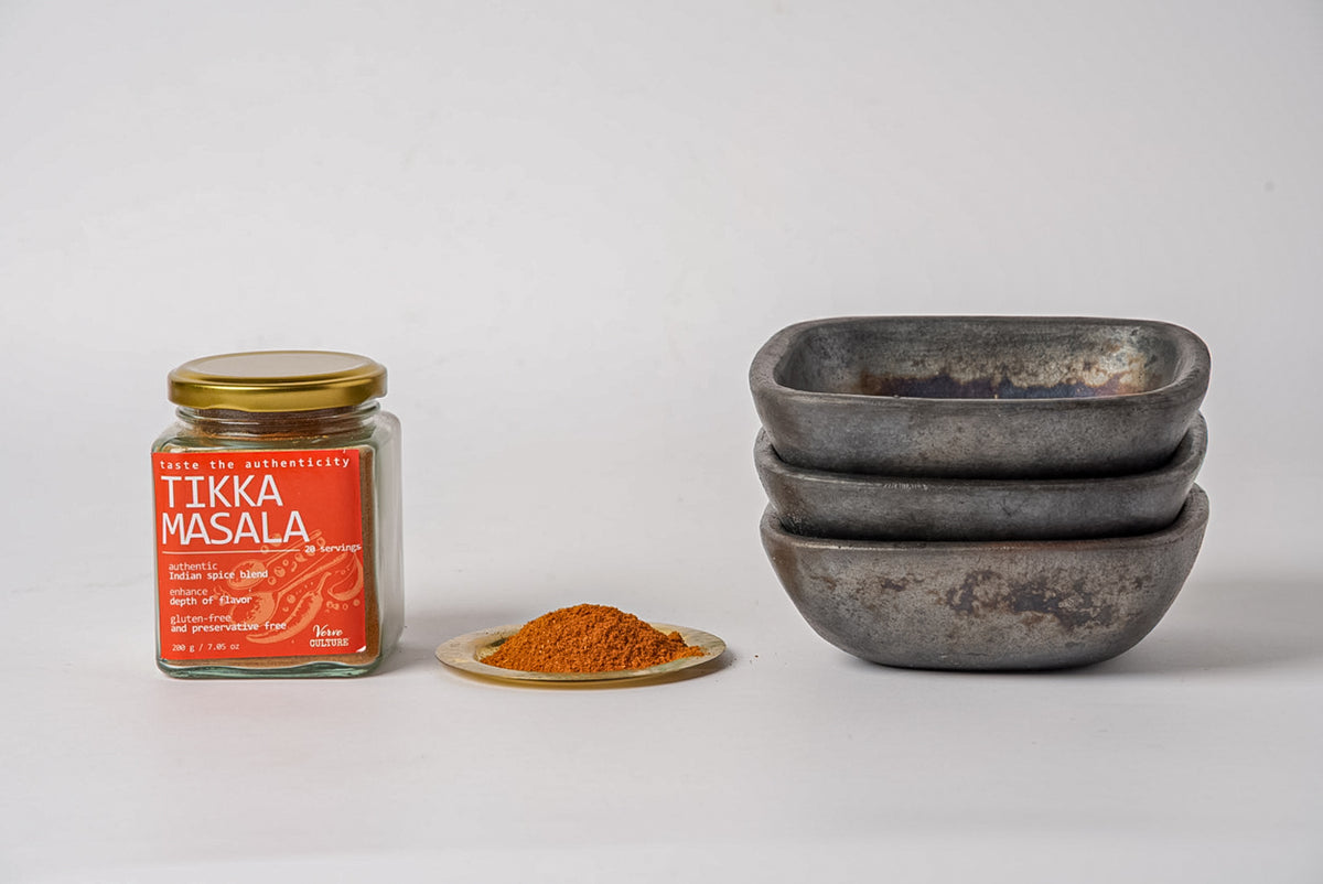 Glass jar with gold lid containing tikka masala spice blend, displayed with a portion of orange-red powder on a small dish an