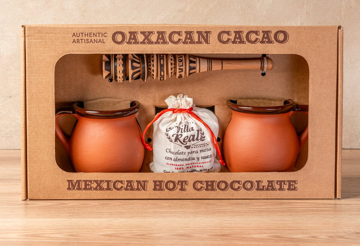Mexican hot chocolate gift set containing two terracotta mugs, wooden whisk, and cloth pouch of chocolate mix.