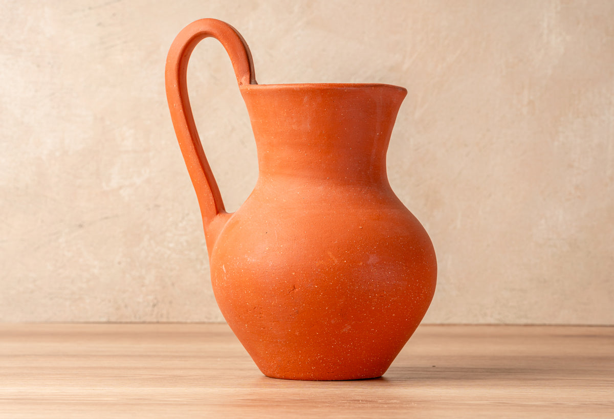 Terracotta jug with curved handle and rounded body in rust-orange color.