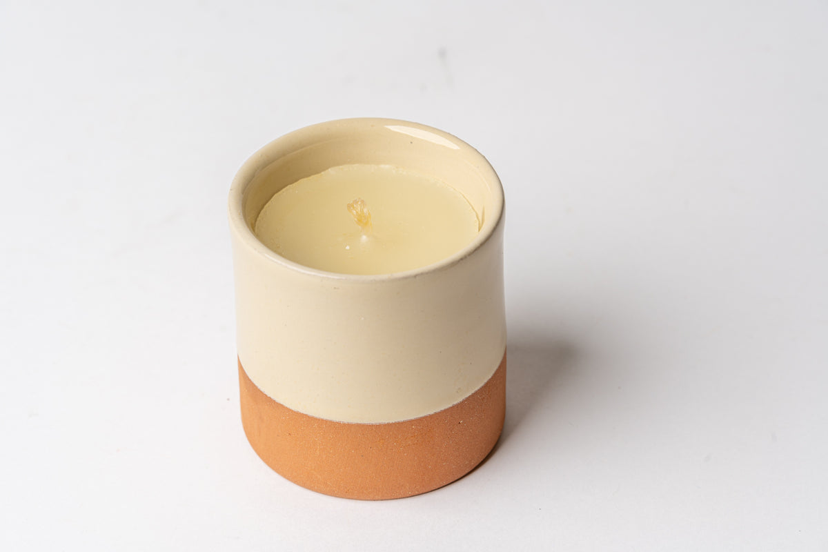 Cream and terracotta two-tone cylindrical candle with single lit wick inside.