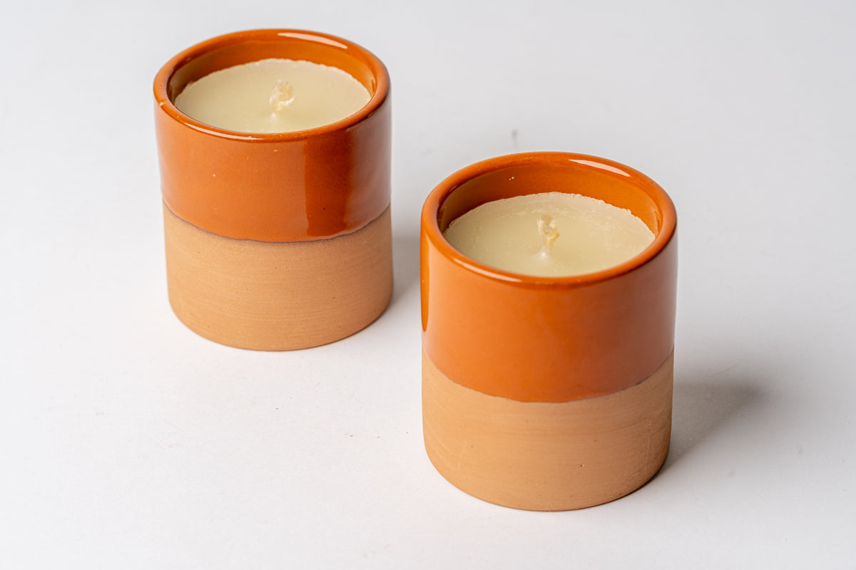 Two cylindrical terracotta candles with cream-colored wax and orange glazed rims.