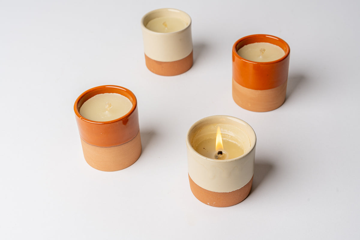 Four cylindrical candles with cream and terracotta-colored ceramic containers, some with visible flames.