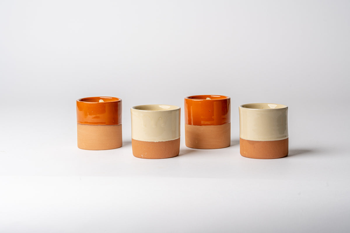 Four cylindrical terracotta candle holders with cream and orange glazed sections arranged in a row.