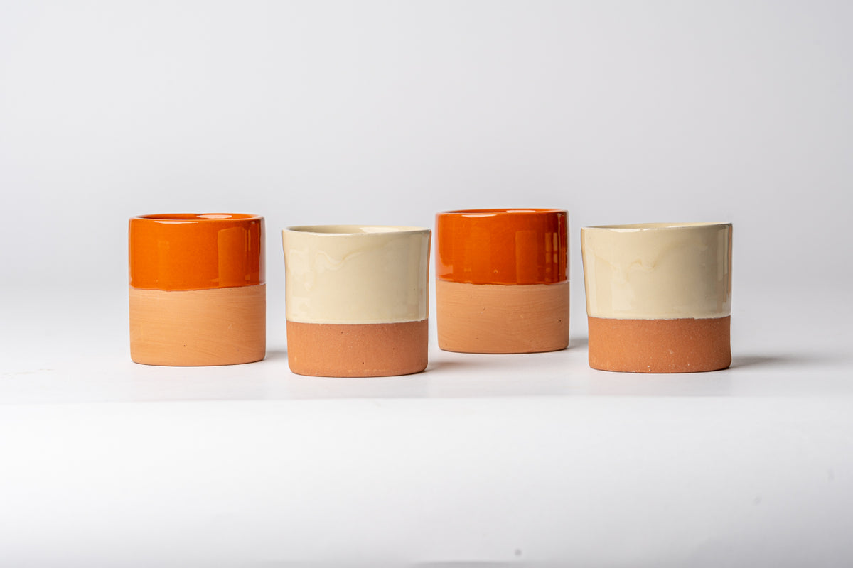 Four terracotta cups with orange glaze tops and natural clay bottoms arranged in a row.