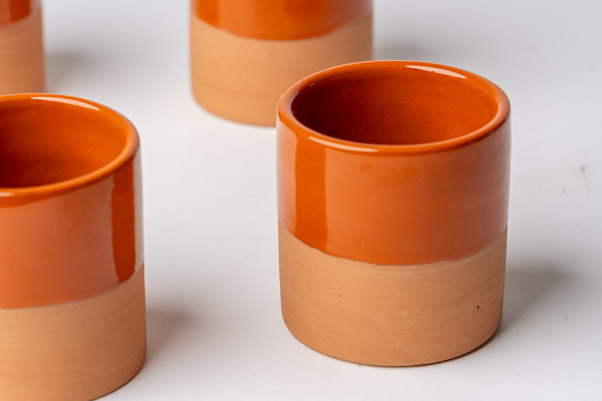 Four terracotta cups with glossy orange-red glazed upper half and matte natural clay lower half.