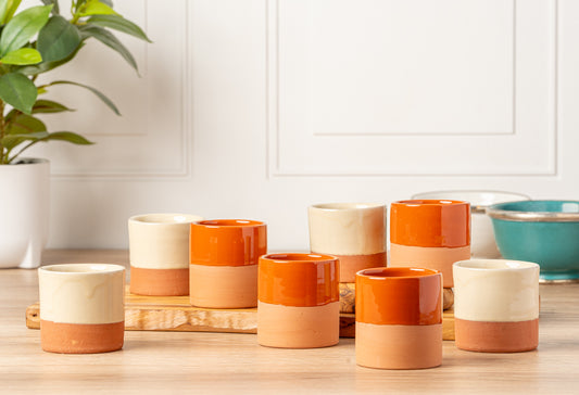 Four terracotta cups with cream and orange glazed sections arranged on wooden surface.