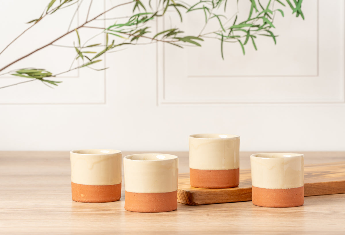 Four terracotta cups with cream-colored upper halves and terracotta lower halves arranged on a wooden surface.