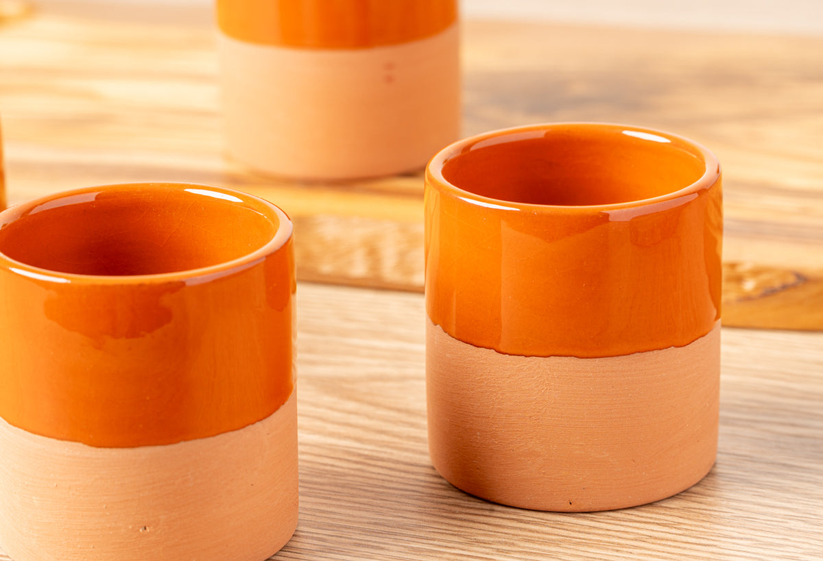 Two terracotta cups with bright orange glazed rims and natural clay bodies on wooden surface.