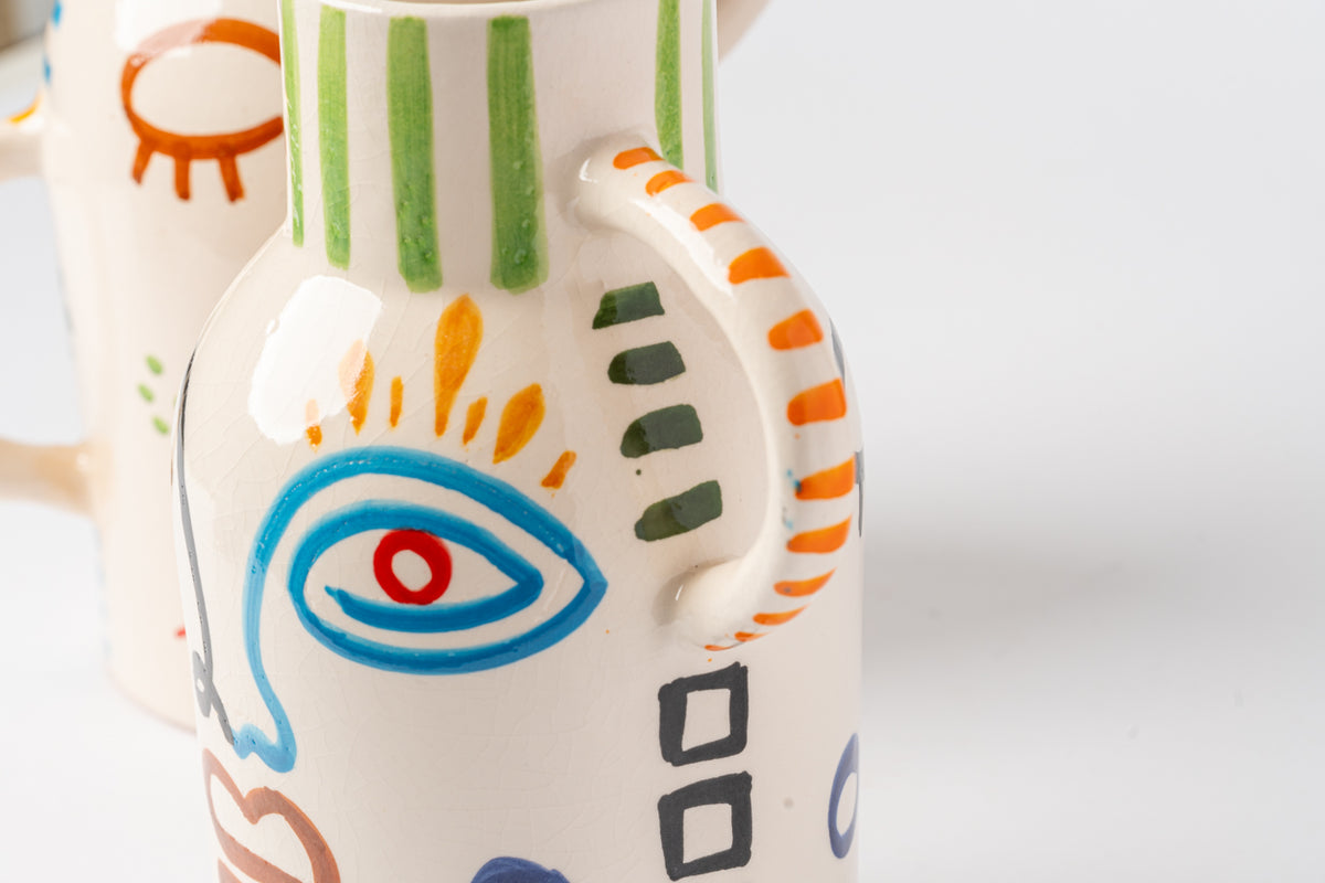 Cream ceramic vase with hand-painted abstract face featuring blue eye, orange and green geometric patterns, and colorful line