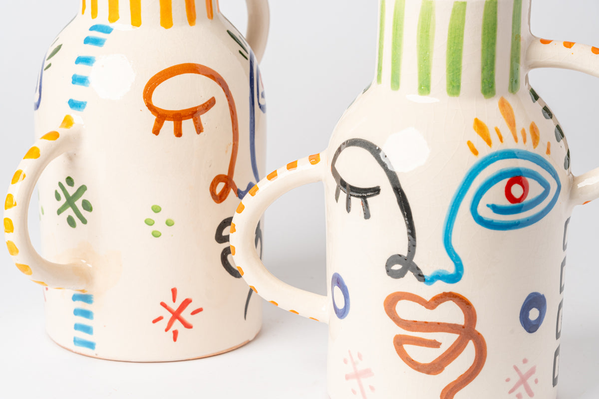 Cream ceramic vase with colorful hand-painted abstract faces and geometric patterns in orange, blue, and green.