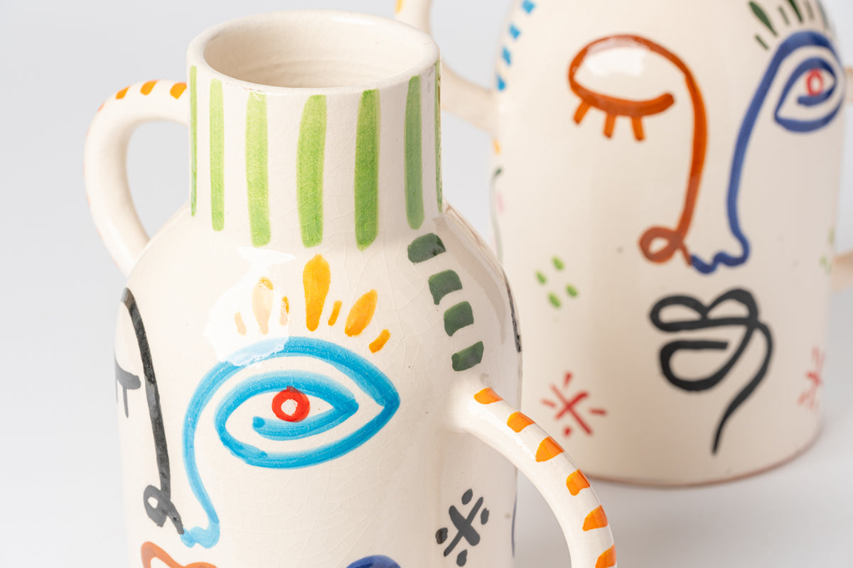 Cream ceramic vase with hand-painted abstract face designs in blue, orange, green and black, featuring geometric patterns and