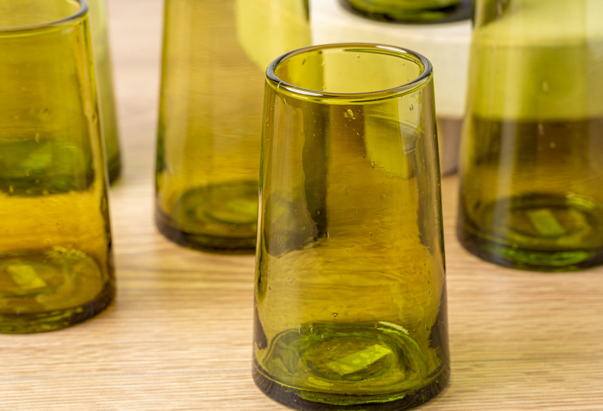 Six yellow-green cone-shaped glasses with gold rims arranged on a wooden surface.