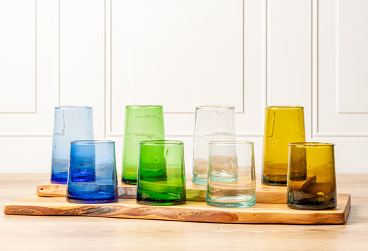 Six cone-shaped glasses in blue, green, clear, and amber colors arranged on wooden coasters.