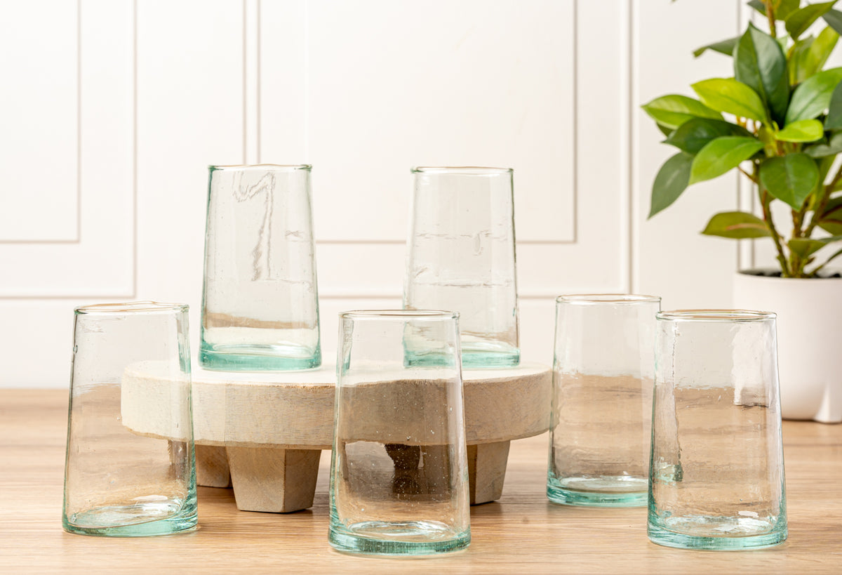 Six clear cone-shaped glasses with turquoise-tinted bases and natural woven holders arranged on wooden surface.