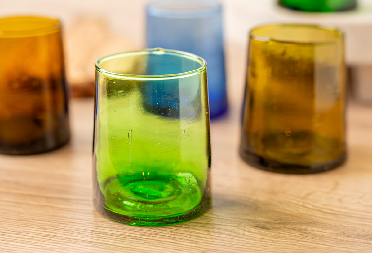 Six colored cone-shaped glasses in green, blue, amber, and yellow tones with beverage inside.