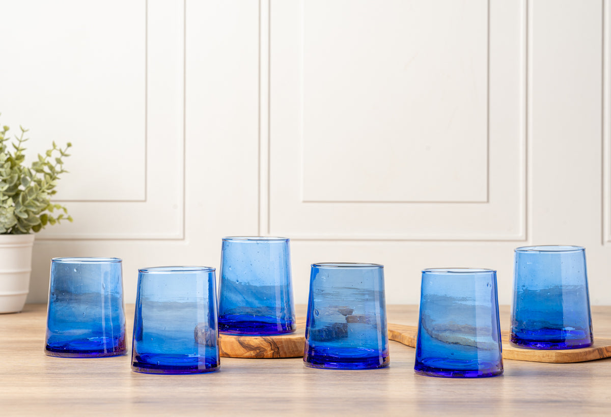 Six blue cone-shaped glasses with gradient coloring from light to deep blue, displayed on a wooden surface.