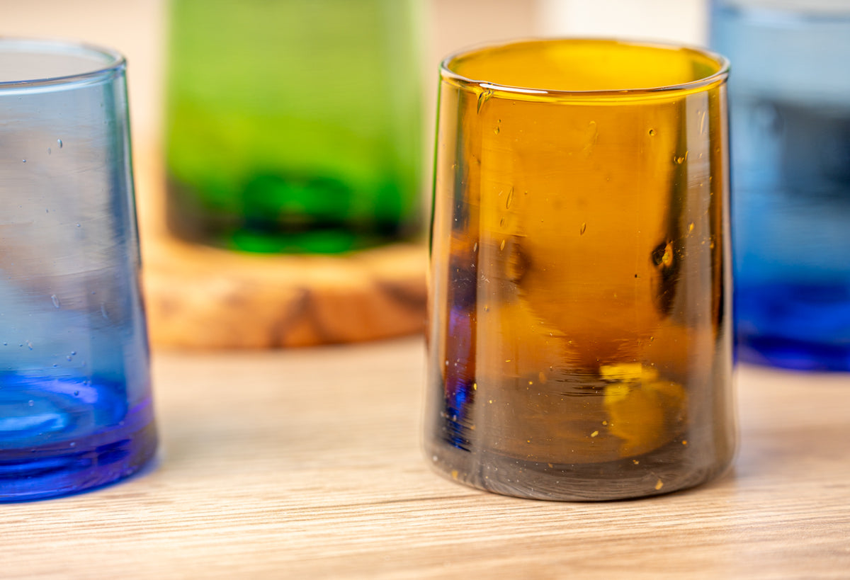 Six colored cone-shaped glasses in clear, green, amber, and blue on a wooden surface.