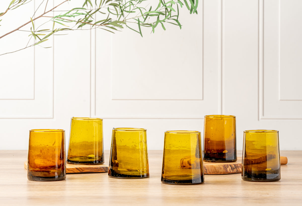 Six amber cone-shaped glasses with tapered bases arranged in a row on a wooden surface.