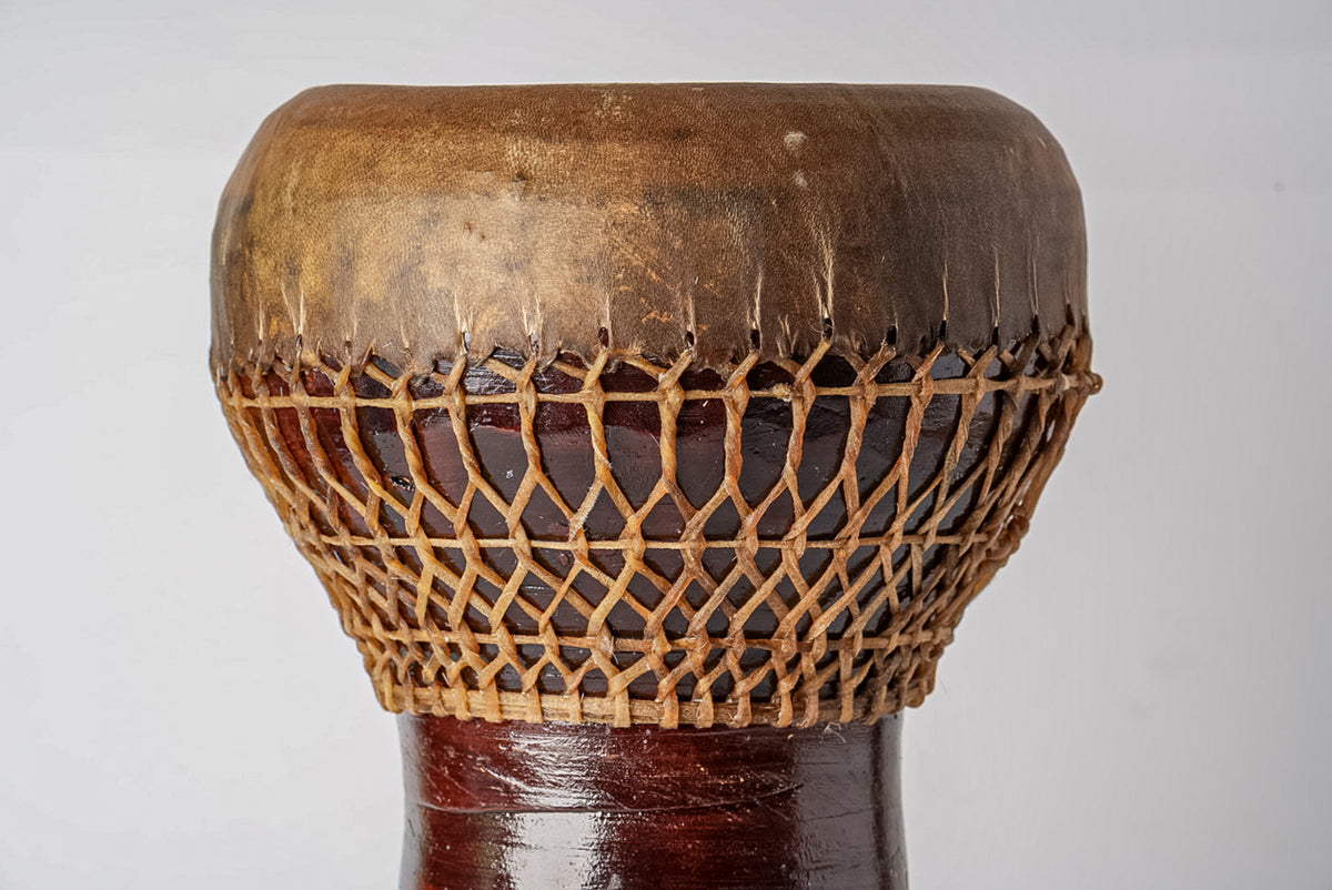 Darbouka drum with brown leather head and woven rope tuning pattern on wooden base.