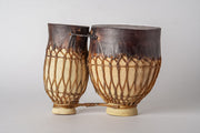 Two goblet-shaped drums with dark leather heads and natural rope tuning, connected by a cord at the top.