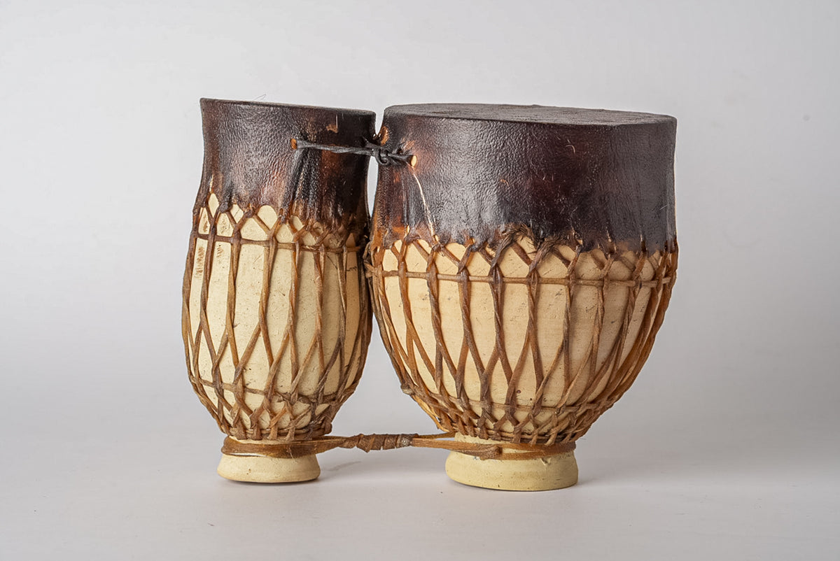 Two goblet-shaped drums with dark leather heads and natural rope tuning, connected by a cord at the top.