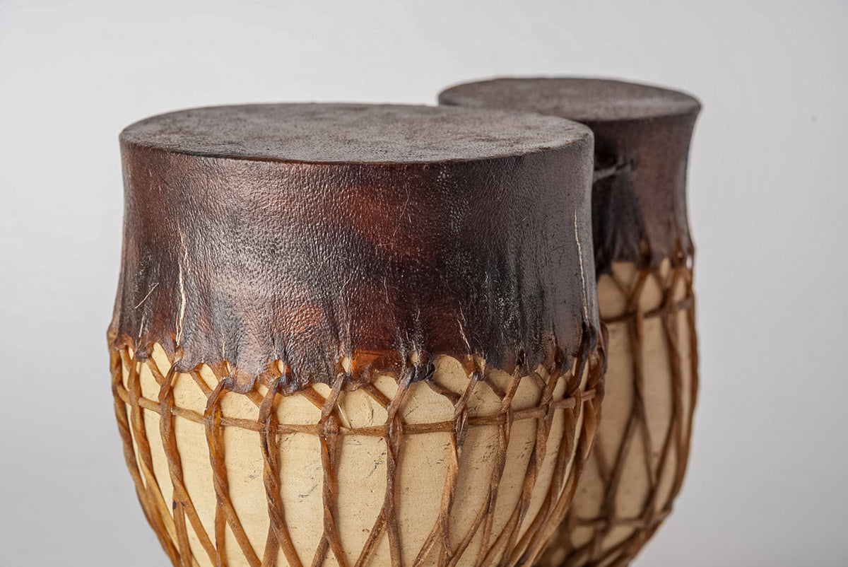 Two brown leather drums with rope tuning and natural wood bases, displayed side by side.