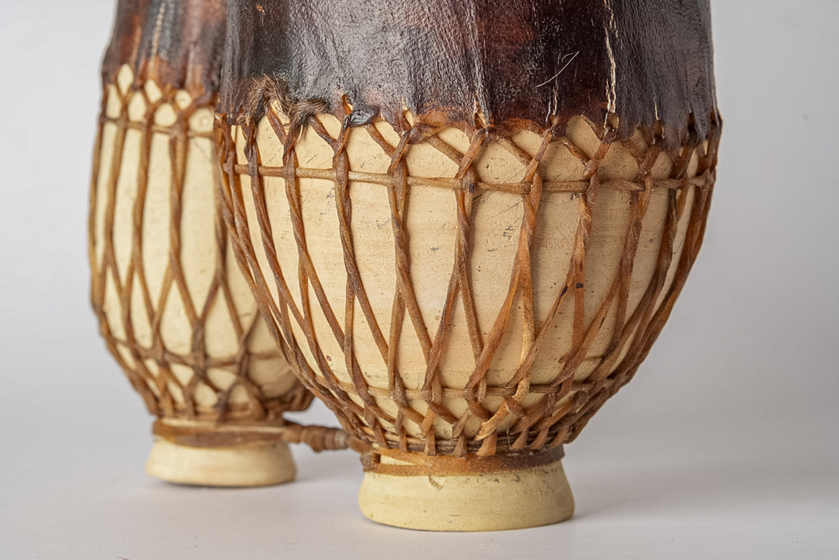 Two wooden drums with rope tuning and dark leather heads, positioned side by side.