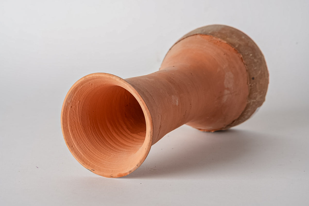 Terracotta drum with cylindrical body and rounded end, hollow interior visible at opening.