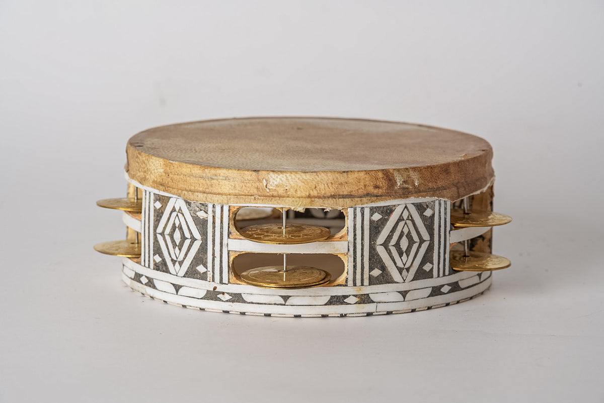 Round wooden tambourine with geometric black and white patterns, metal jingles, and brass handles on sides.