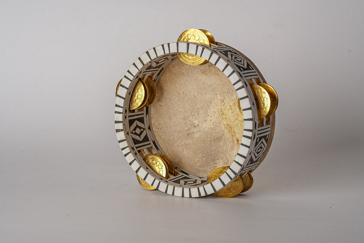 Round tambourine with natural parchment head, decorative metal rim with geometric patterns, and brass jingles positioned arou