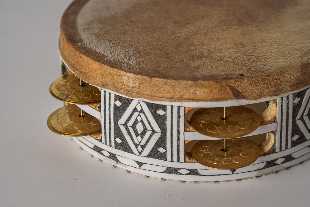 Round tambourine with tan fabric head, wooden frame, brass jingles, and decorative woven band with geometric patterns.