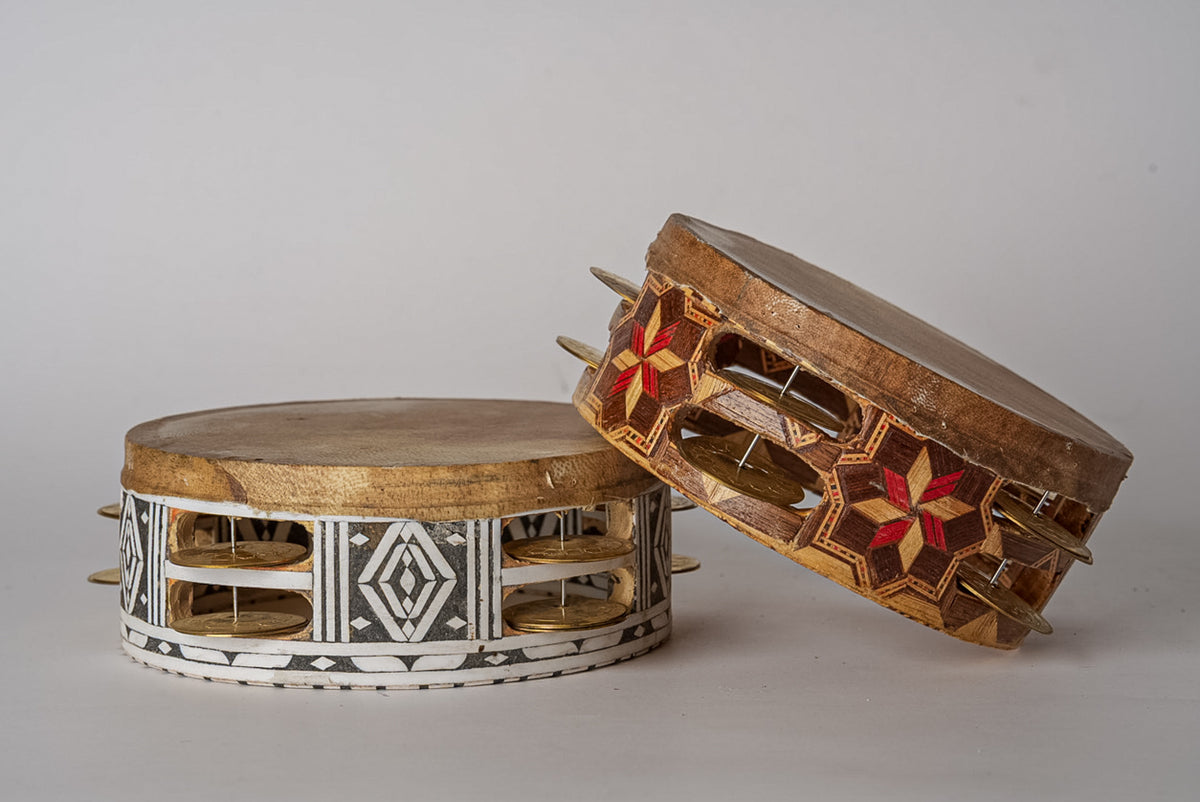 Two wooden tambourines with metal jingles, one with white and black geometric patterns, one with brown finish and red floral 