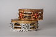 Two wooden frame drums with metal jingles, decorated with geometric patterns in red and white inlay, stacked together.