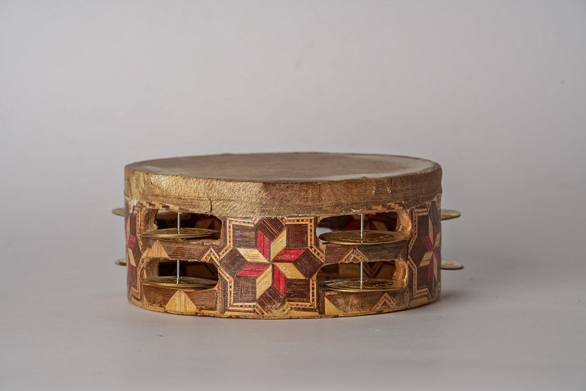 Wooden tambourine with inlaid red and gold geometric patterns, metal jingles on sides, and natural hide drumhead on top.