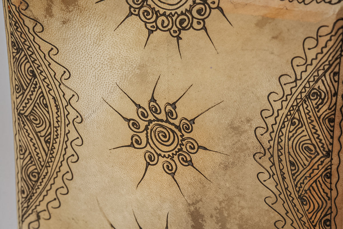 Square drum head with tan leather surface decorated with black henna-style spiral and geometric patterns.