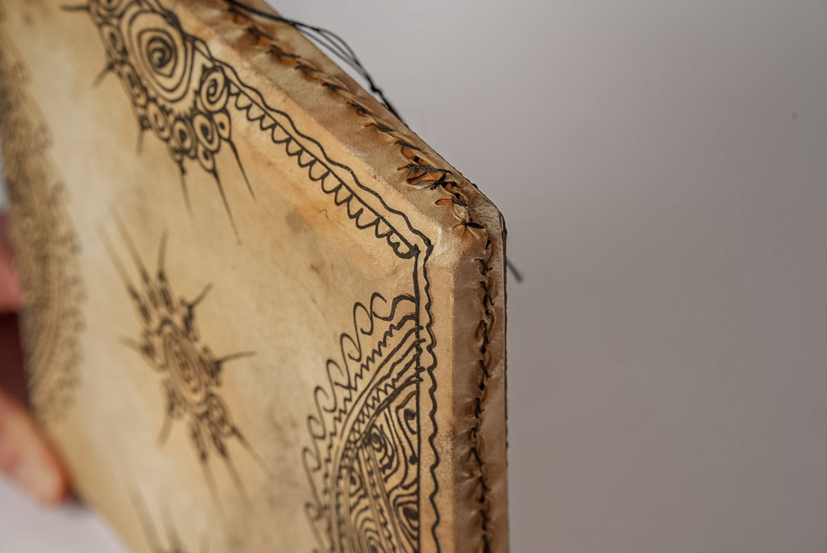 Square wooden drum with burnt decorative geometric patterns and scrollwork designs on natural surface.