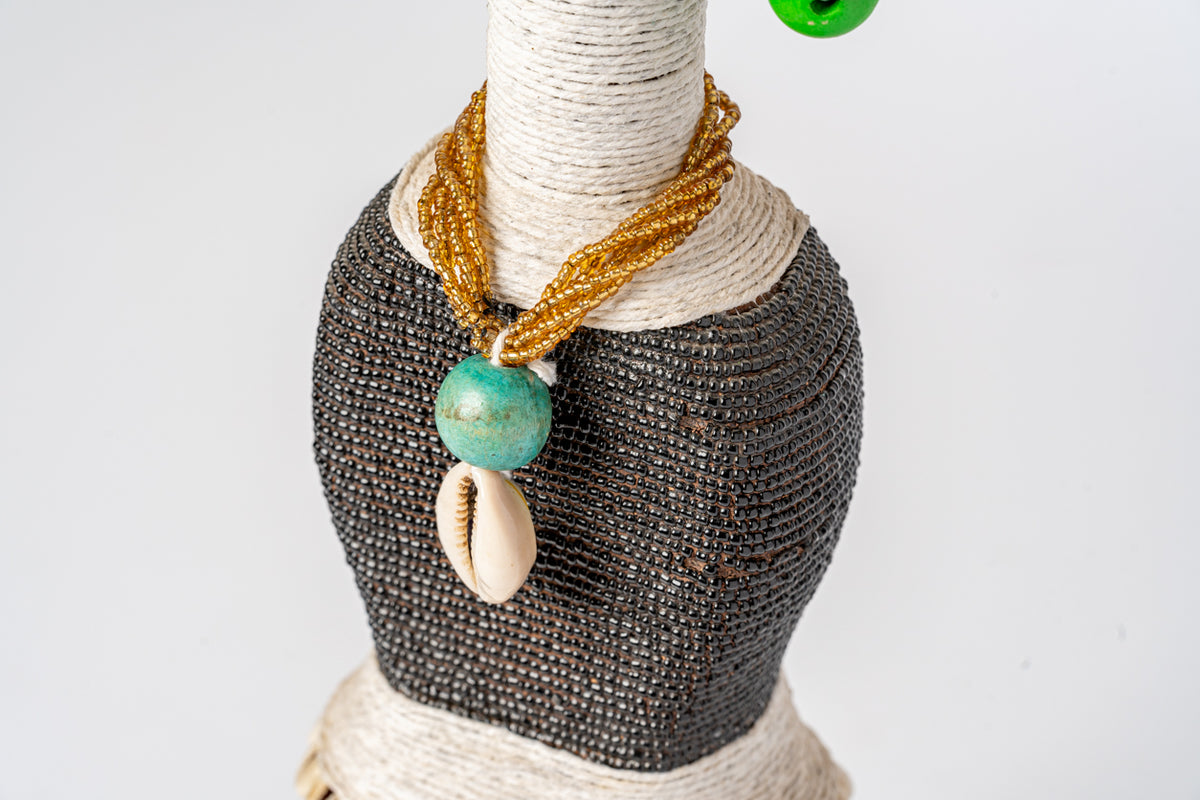 Doll with wrapped rope head, dark beaded body, gold cord necklace, turquoise bead, and shell pendant.