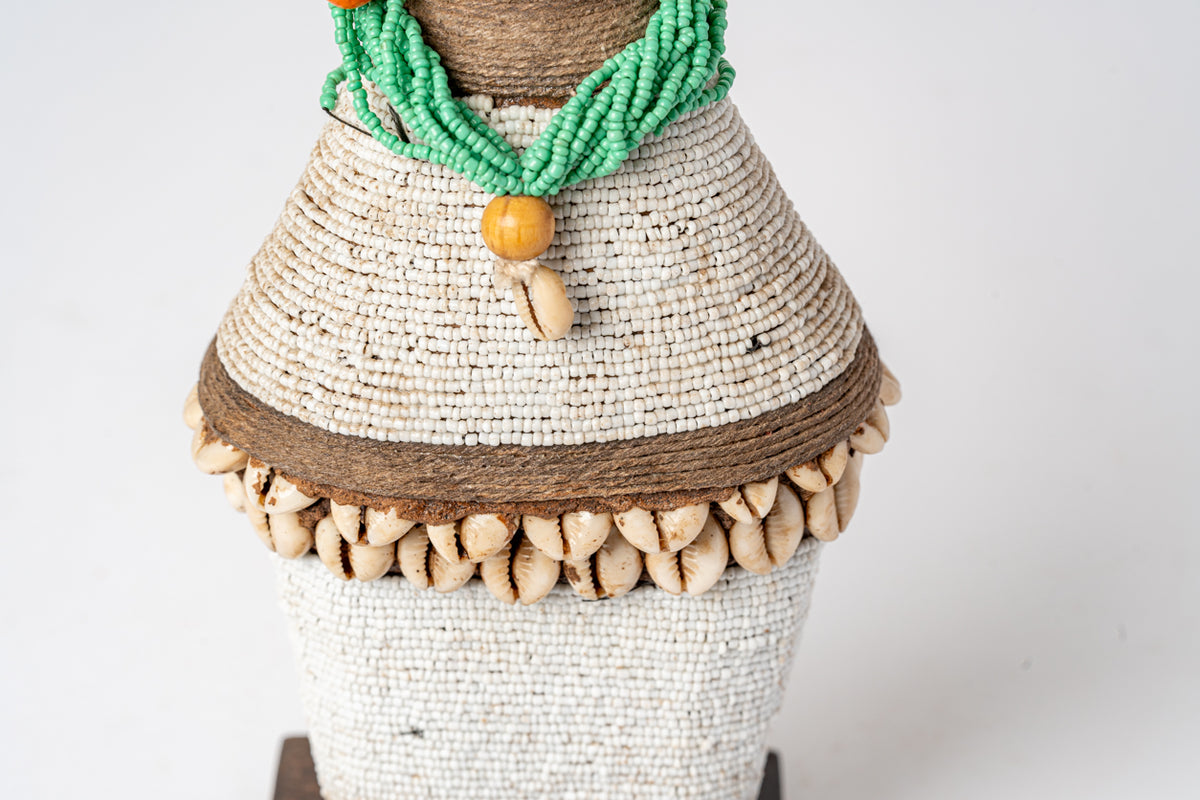 Handcrafted doll with beaded cream and white body, brown wrapped waist, green beaded necklace, and wooden bead pendant.