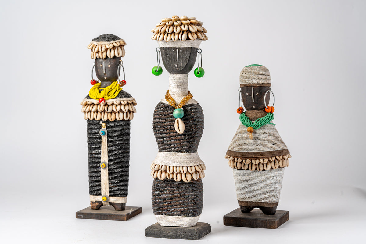 Three decorative dolls with wooden beaded headdresses, wrapped textile bodies, and colorful beaded accessories on wooden base