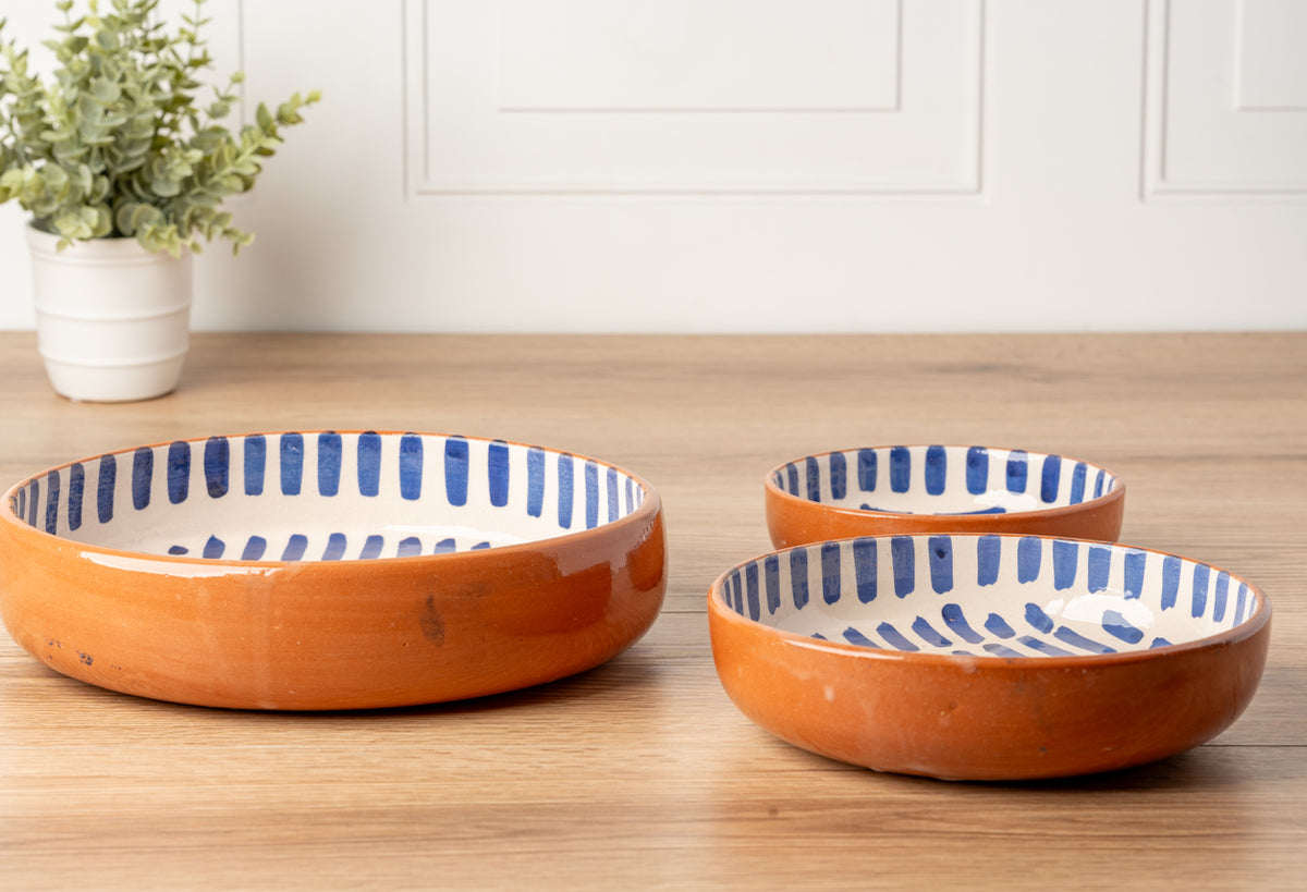 Three nesting bowls with orange exteriors and blue stripe interiors on wooden surface.