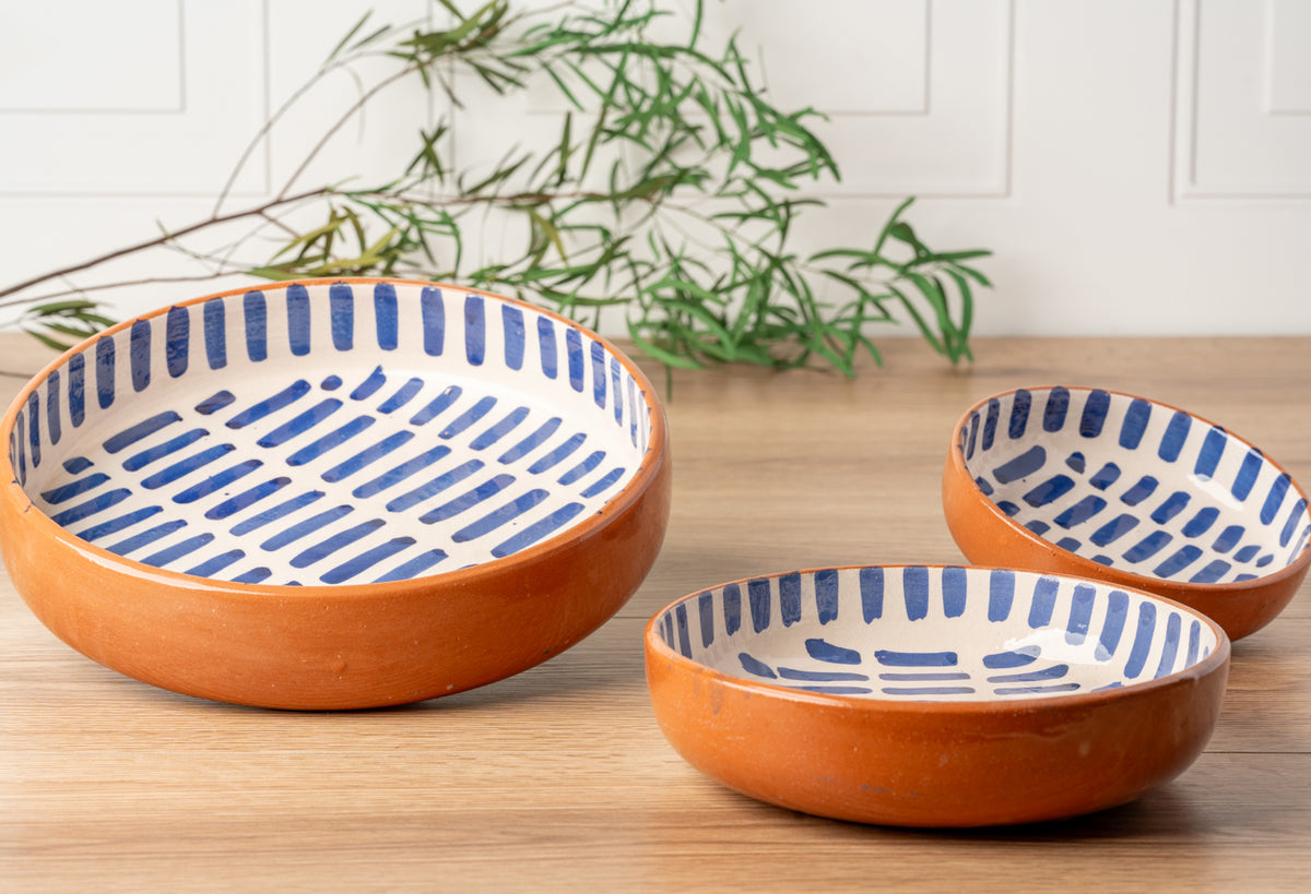Three nesting dishes with orange exterior and blue stripe pattern interior on wooden surface.