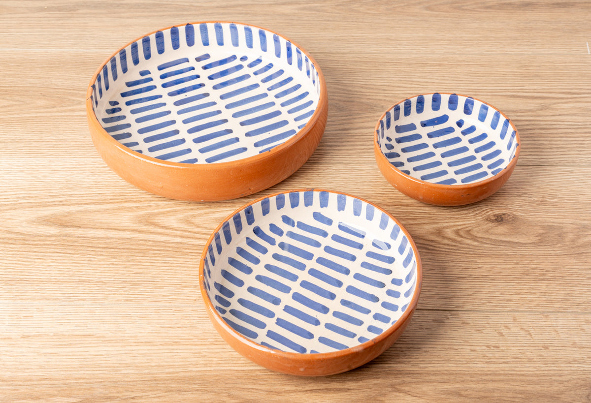 Three ceramic nesting bowls with orange exterior and blue striped interior pattern on wooden surface.