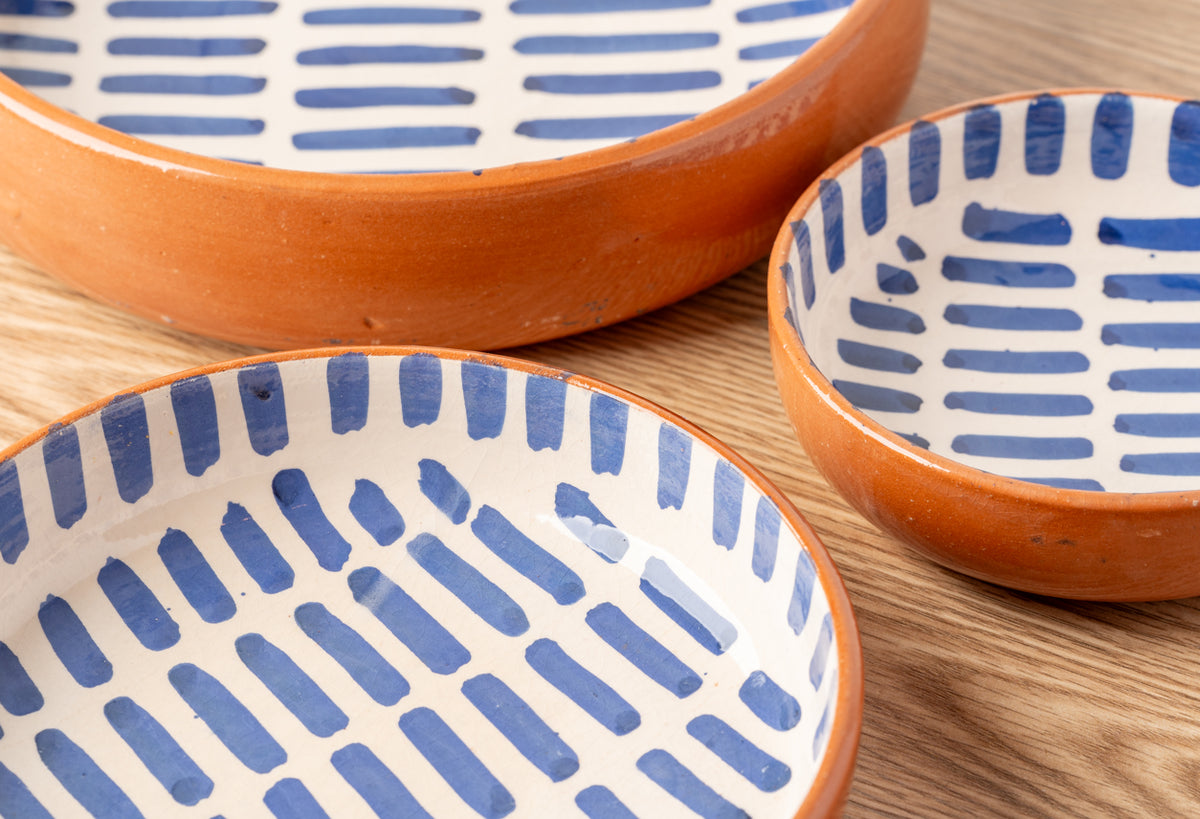Three ceramic nesting dishes with terracotta rims and white interiors decorated with blue stripe patterns.