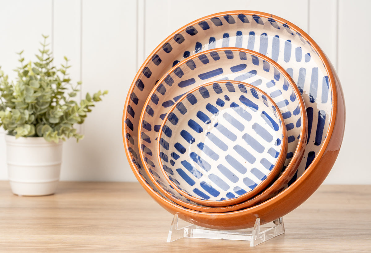 Three stacked nesting bowls with terracotta rims and blue striped interior pattern on wooden surface.