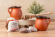 Two terracotta pitchers, wooden whisk, chocolate tablets, and packaged mix arranged on a white ceramic tray.