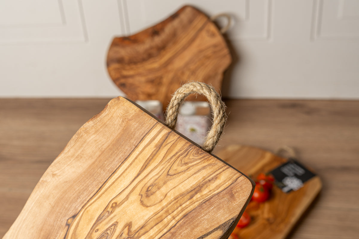 Wooden charcuterie board with natural grain pattern and twisted rope handle in foreground, additional boards blurred in backg