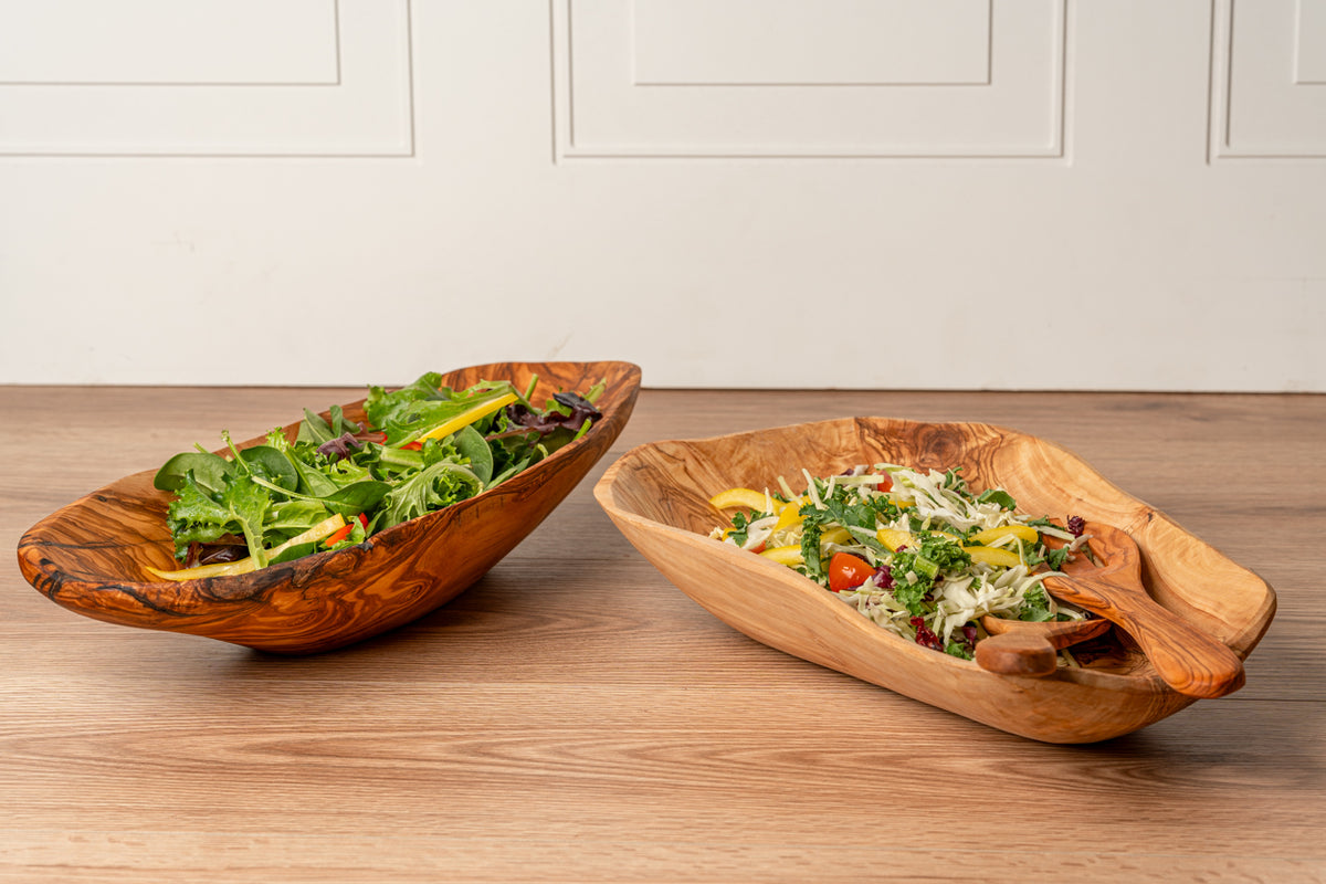 Two wooden bowls with natural grain patterns, each filled with fresh salad containing greens, vegetables, and toppings.