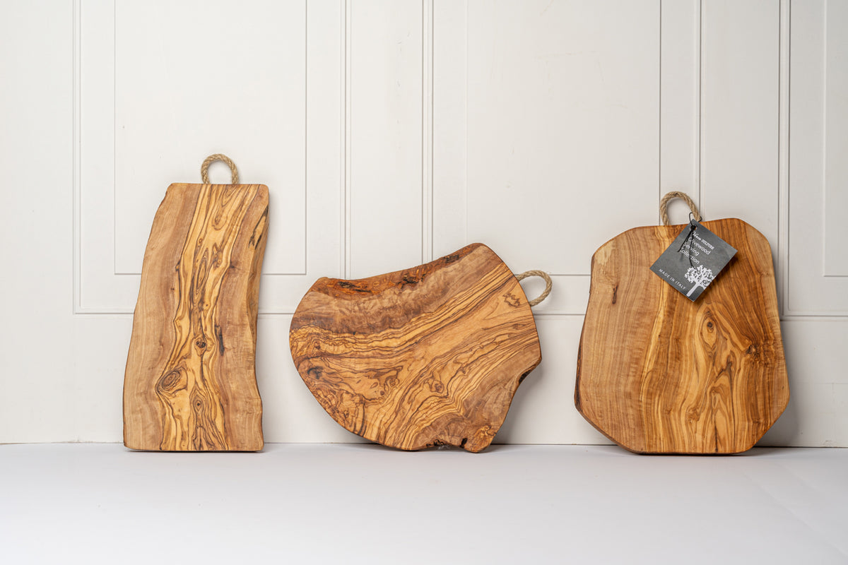 Three olivewood charcuterie boards with rope handles in varying shapes and wood grain patterns.