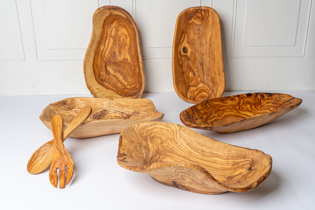Olivewood bowls and serving utensils with natural grain patterns and irregular edges in various organic shapes.